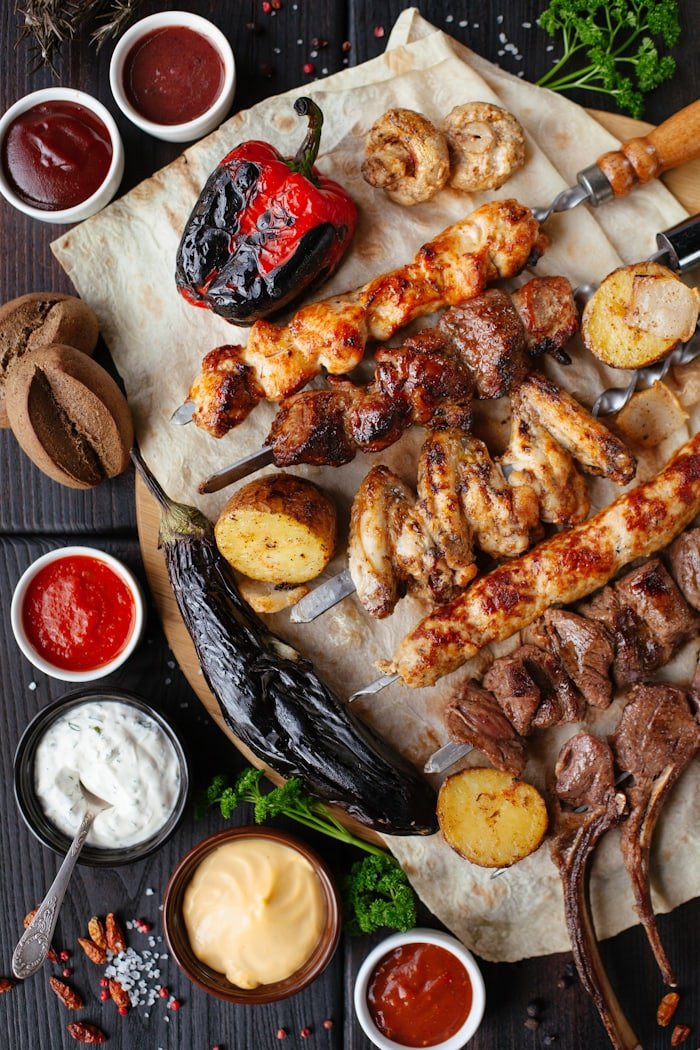 Grilled lamb chops and beef skewers on a board with sauces